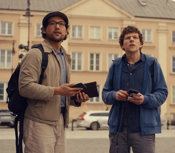 Jesse Eisenberg and Will Sharpe look up at something in the sky while standing on a city street.