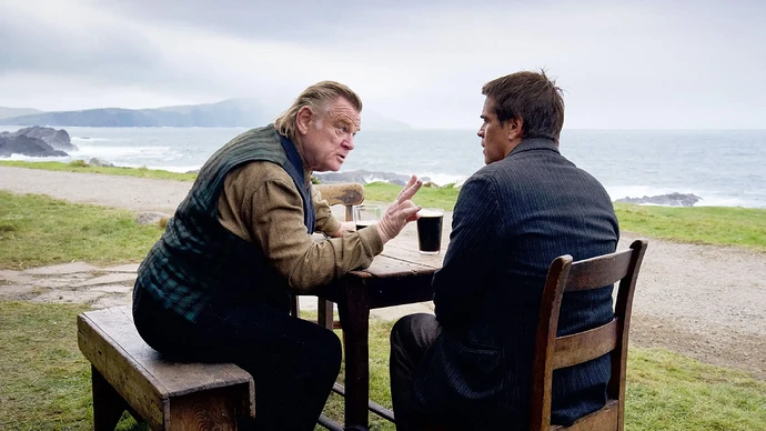 Brendan Gleeson and Colin Farrell sitting at a table outdoors by the sea.