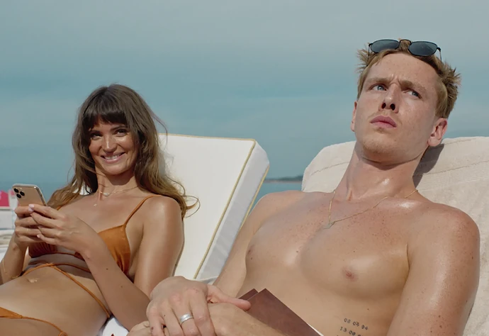 A man and woman relaxing on a yacht, the woman is smiling and looking at her phone.