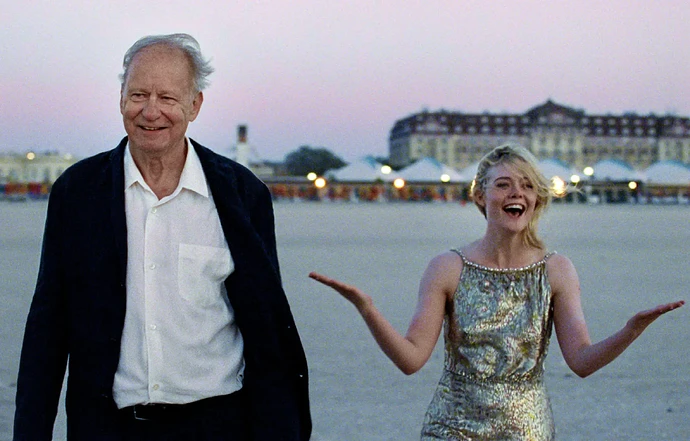 Stellan Skarsgård and Elle Fanning walking on a beach at dusk.