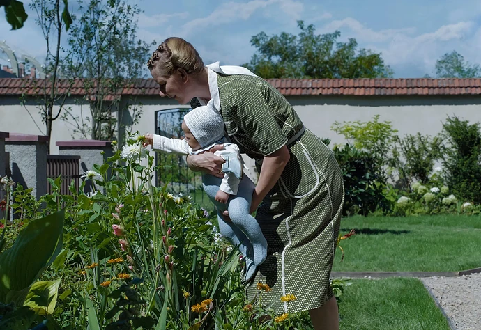 Sandra Hüller as Hedwig Höss holding a baby to smell flowers in a garden next to the Auschwitz concentration camp.