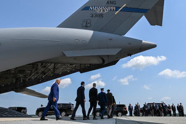 President Trump, Defense Secretary Pete Hegseth and a line of American officials walking on a tarmac near the back of a U.S. military transport plane.