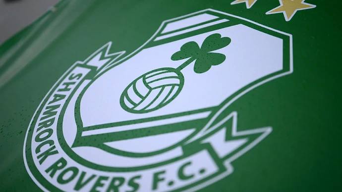 The Shamrock Rovers crest, with two stars signifying the club's 20th league title, on a green surface.